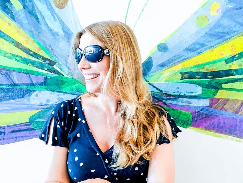Abigail King from Inside the Travel Lab sitting wearing her sunglasses in front of painted colourful wings