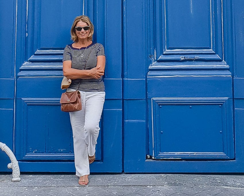 Suzanne Jones - The Travelbunny standing outside blue doors wearing a striped top and grey trousers