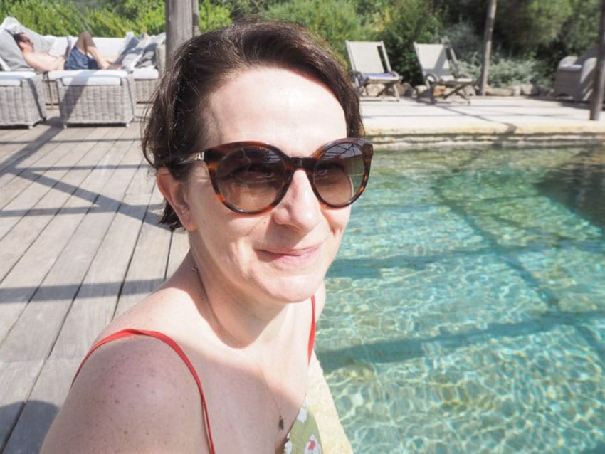 Stephanie from From the Poolside sitting beside a swimming pool wearing sunglasses