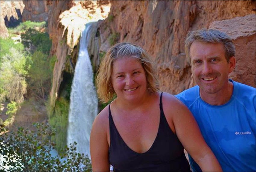 Jenn in a black strappy vest top and Ed in blue t-shirt  from Coleman Concierge with Hualapai Hilltop and waterfall in the background