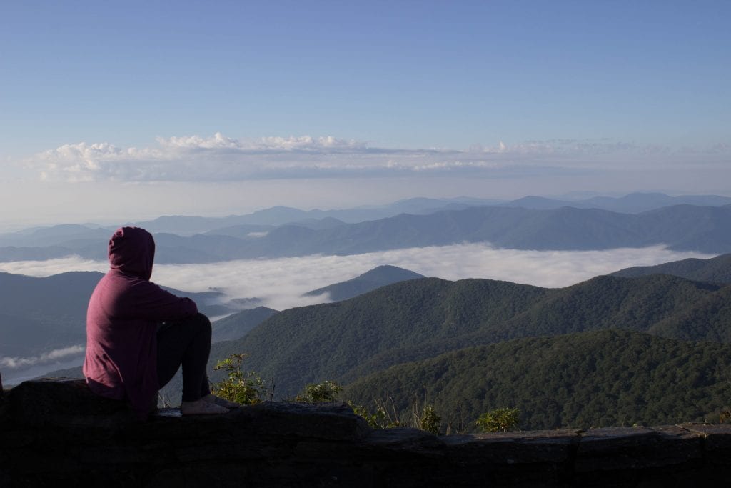 Woman in a purple hoodie with hood up looking out over fog covered hills