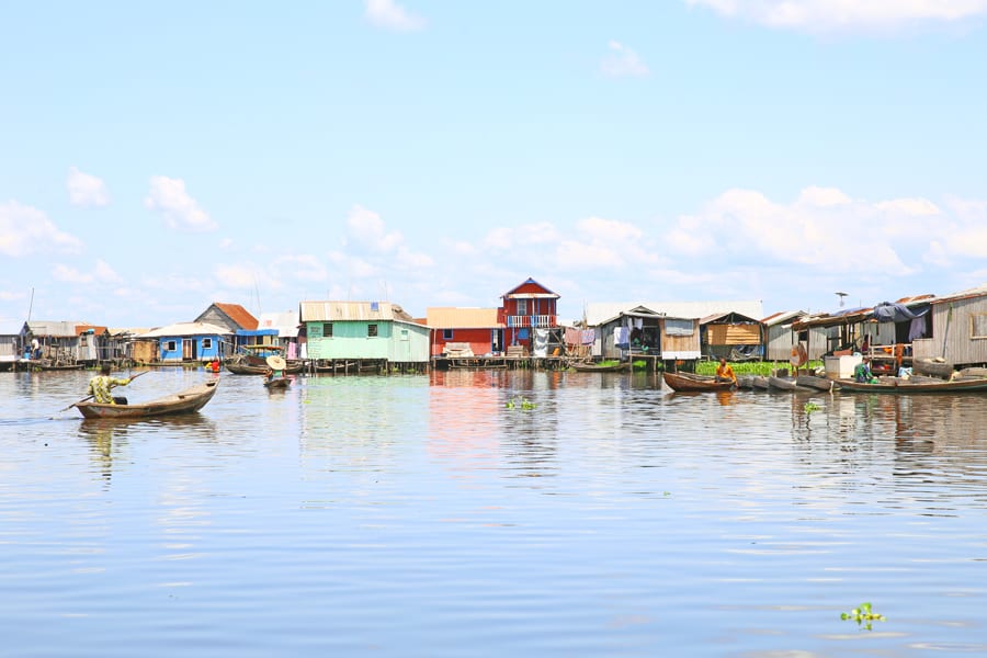 blue lake with a row of colourful houses in blue, green and red on stilts with wooden canoes on the lake