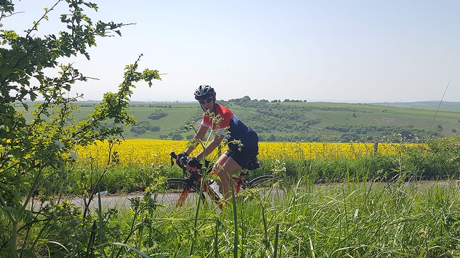 lady on bicycle wearing a crash helmet and cycling on a road through green fields and yellow rape fields
