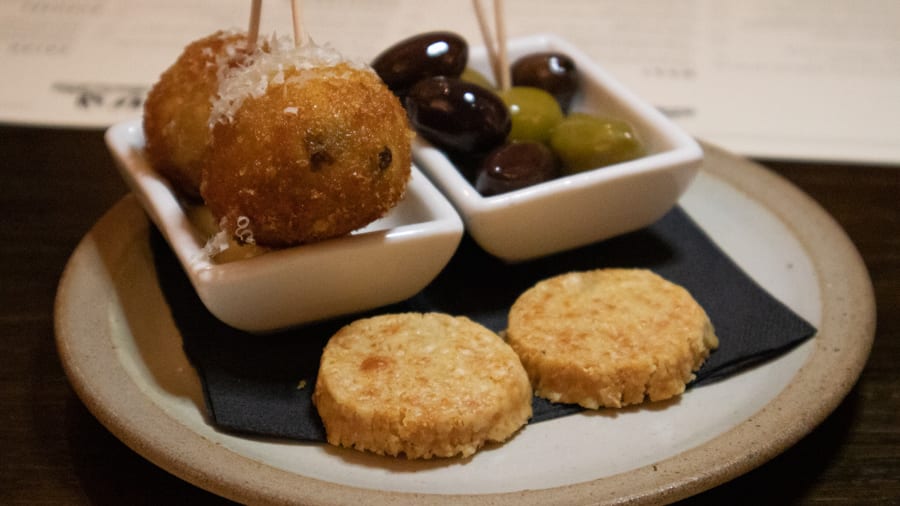 Two arancini balls, green and black olives and parmesan crisps on a black napkin on a stone coloured plate