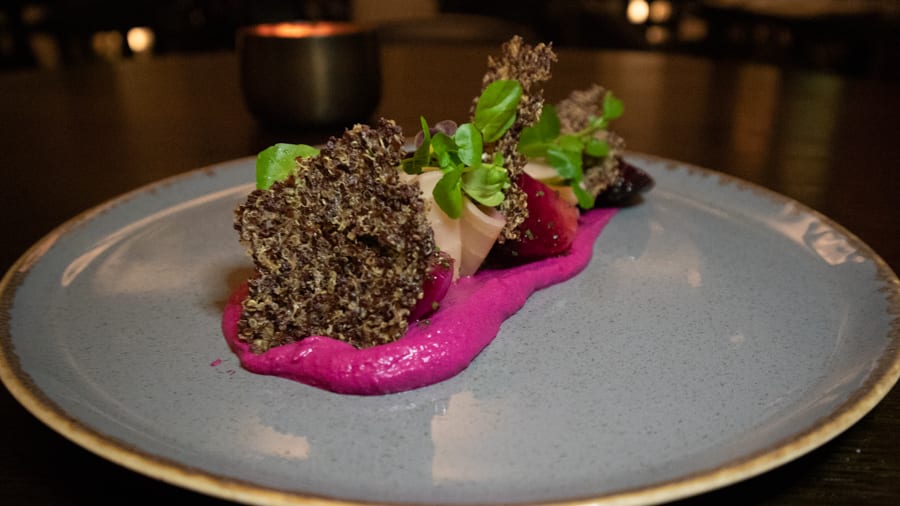 blue plate with bright pink beetroot hummus topped with rainbow beetroot, quinoa crisp and microgreens