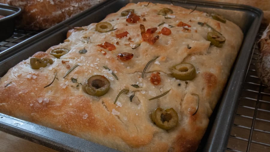 rectangle cooked bread topped with olives, rosemary, salt and sundried tomatoes