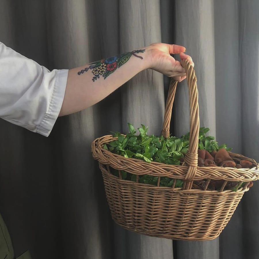 woman's arm with tattoo holding a basket of vegetables