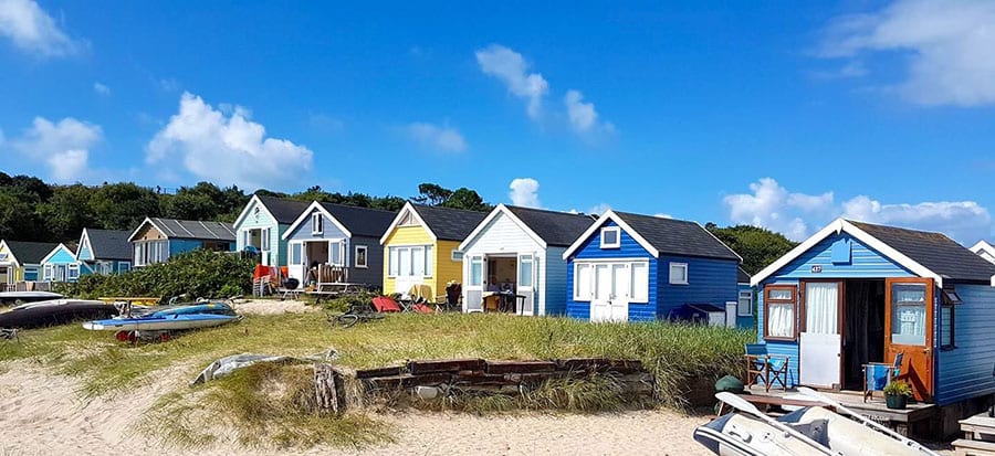 A row of different painted beach huts with grass and sand in front