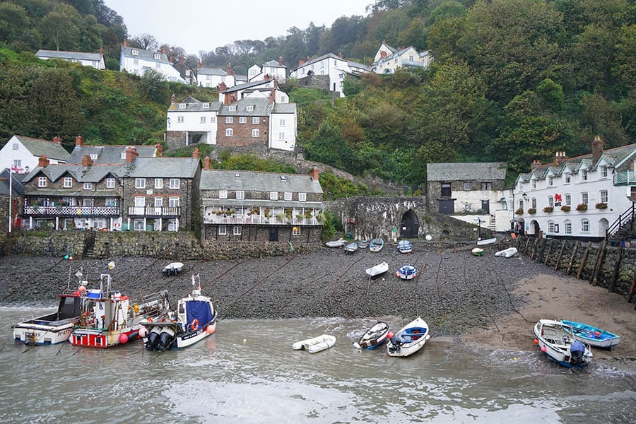 View from the sea of Clovelly. Boats tied up on long ropes with a dark beach and houses going up the hill