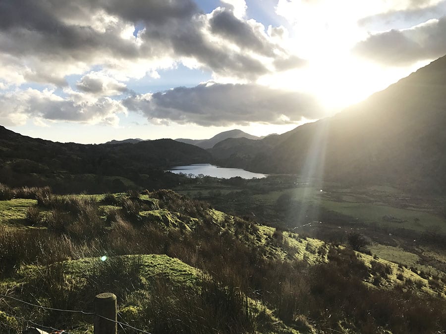 hills surrounding a lake in Snowdonia with the sun coming out behind the clouds