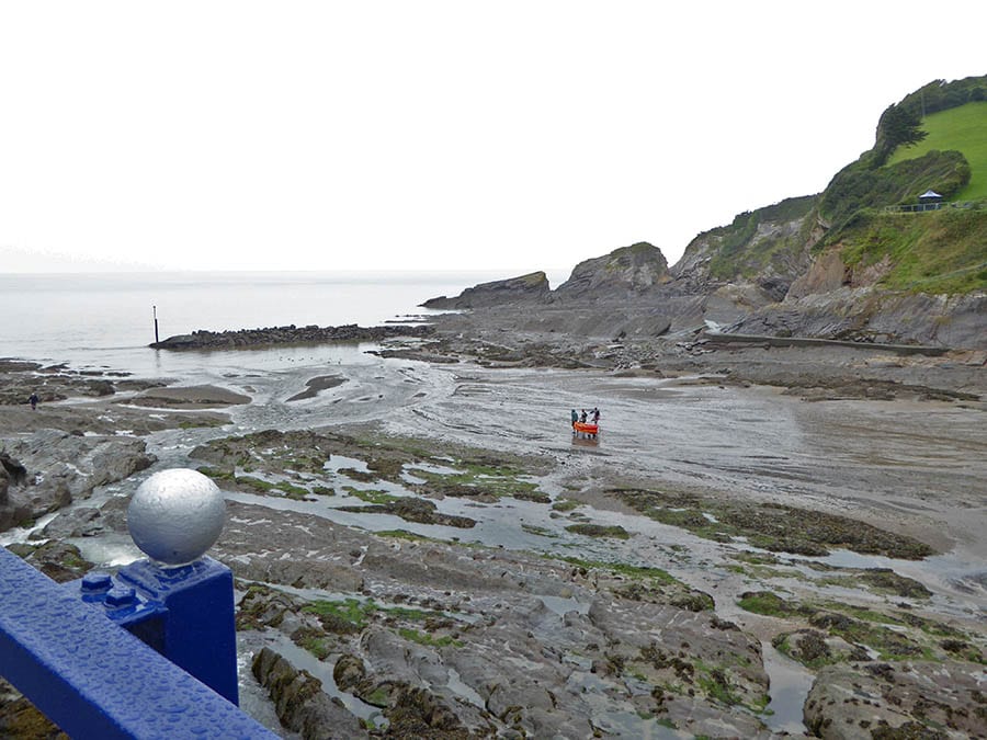 beach at Coombe Martin with tide out and 3 men taking an orange kayak out to sea