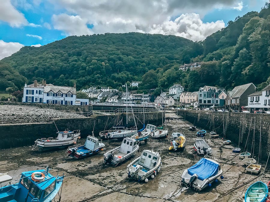 Lynton and Lynmouth harbour. The tide is out and the boats are resting on the ground. Thee are houses and mountains around