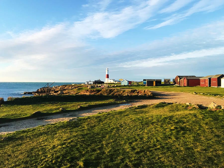 image looking over grass towards the lighthouse at Portland Bill with sea on the left and buildings on the right