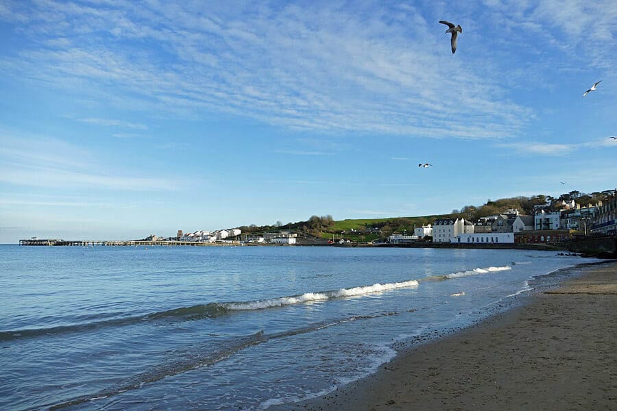 The beach at Swanage with the tide coming in and white houses in the background and blue skies.