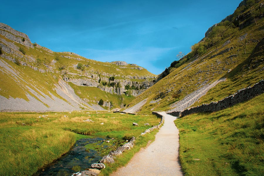 path leading through Gordale Scar with grass covered side and a burn running through it