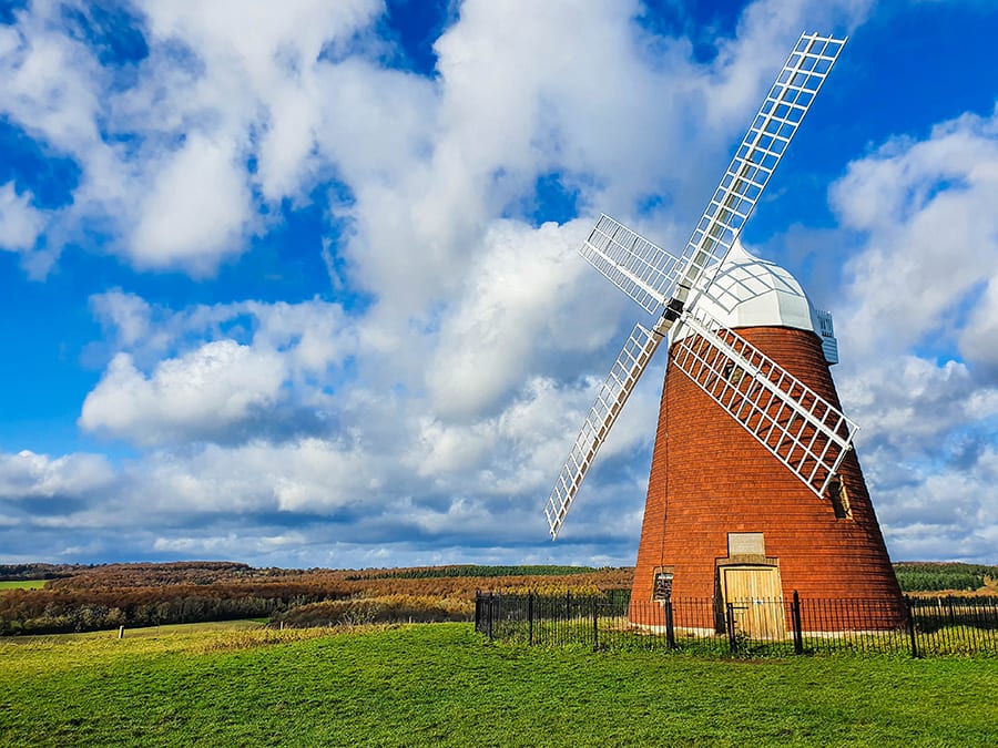 Halnaker Windmill, a red brick windmill with white top and white lattice sails surrounded by a black fence in a green field