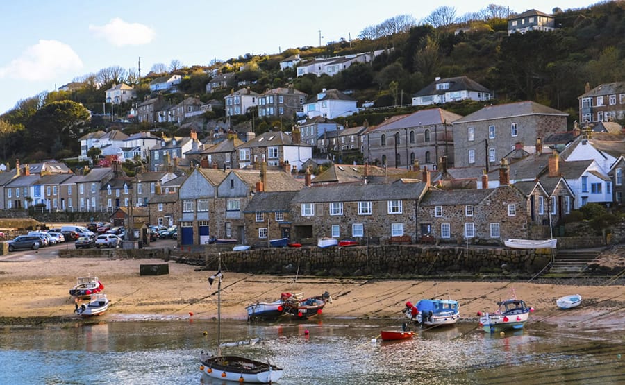 rows of houses going up a hill with a sandy beach in the foreground with boats on it