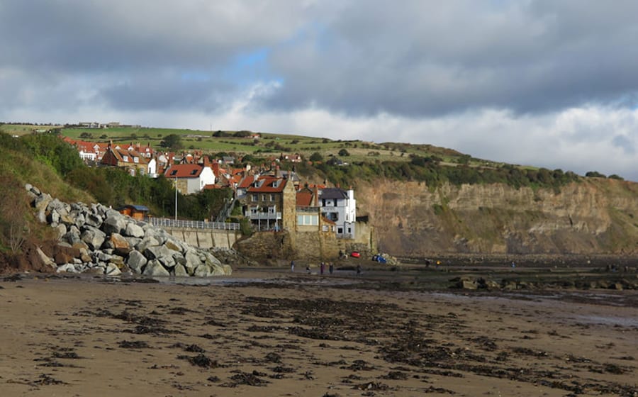 sandy beach with seaweed in the foreground and houses on the edge of a cliff in the background