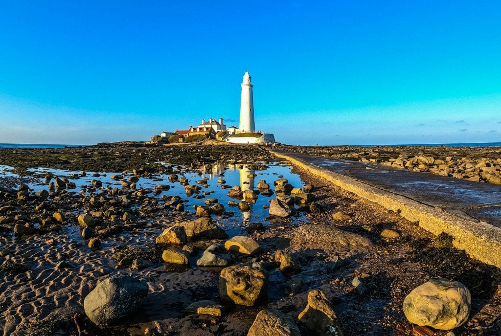 white light house with the tide out. A causeway divide the rocks and rockpools