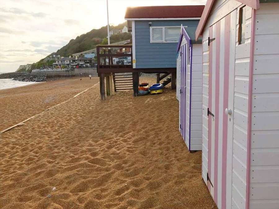 Sandy beach with painted beach huts, white with white and pink stripe door and white with white and purple stripe door