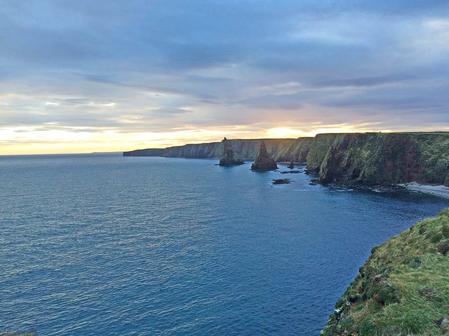 sea with view over grassy hills to Duncansby Stacks in the distance