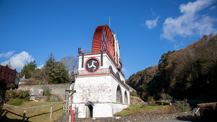 Large red waterwheel with white brickwork and Isle of Man three-legged man on the front