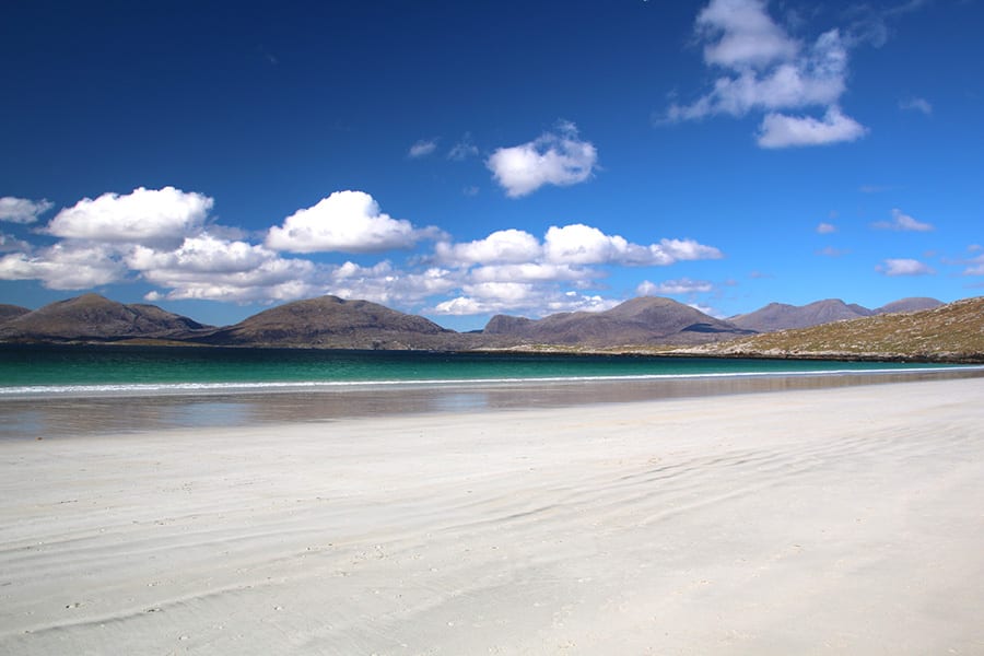white sandy beach with green sea and hills in the background