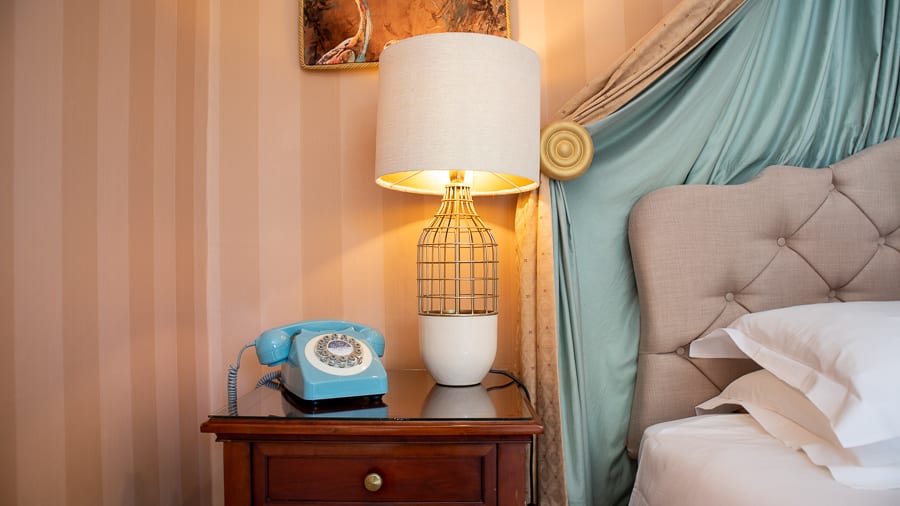 blue old fashioned dial phone next to lamp with open weave base and pale blue silk headboard