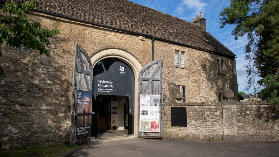 Lacock Abbey and Fox Talbot Museum Ticket Office with large open barn doors and a large black leaf sign saying Welcome to Lacock