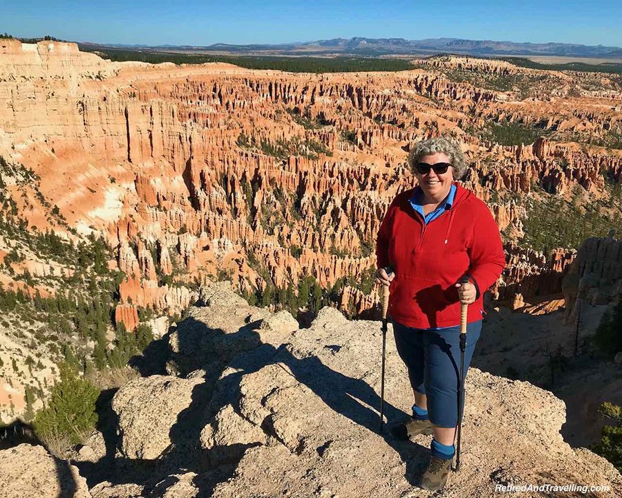 Linda from Retired and Travelling wearing a red sweatshirt and blue trousers with the Bryce Canyon National Park Viewpoints behind her
