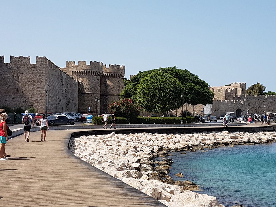 Palace of The Grand Master in Rhodes, Greece with a wide boardwalk in front, above white rocks and sea