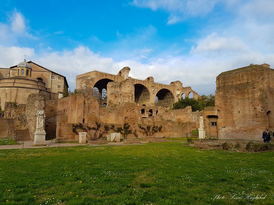 The ruins of the Roman Forum with three large arches and statues