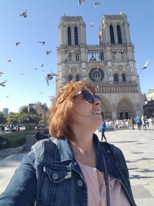 Susan from GenXTraveler with a cathedral behind her an pigeons flying around
