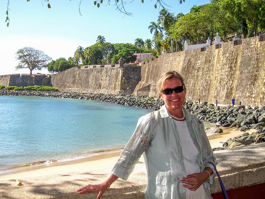 Amy from The Travelling Tulls' in Puerto Rico leaning against a wall with the sea behind her