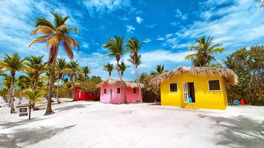 brightly painted beach shacks in yellow, pink and red surrounded by palm trees on white sand