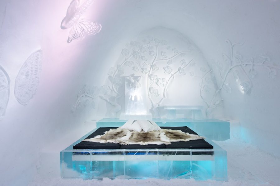 inside Ice hotel with ice butterflies and decoration on the walls and a carved iced bed with mattress and reindeer blanket