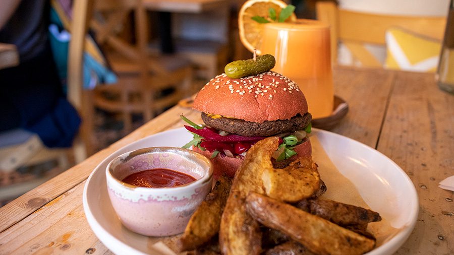 Vibe Pink Burger with beetroot and bean patty, onion,s pink beetroot bun, chilli sauce and Manx potato chips with a ginger and carrot drink at Vibe on of the vegan restaurants in the UK