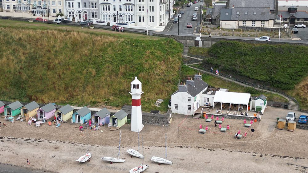 Foraging Vintners & Noa Bakehouse at the Cosy Nook, Port Erin beach with red and white lighthouse, pastel painted beach huts