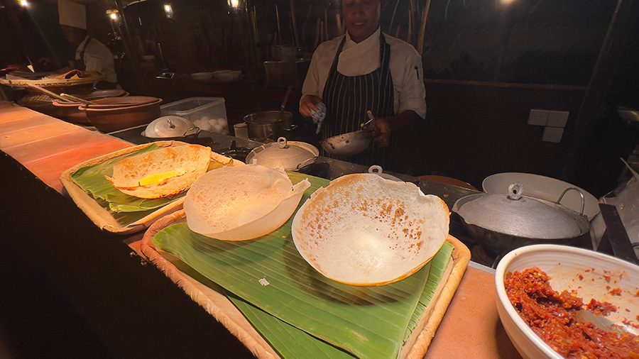 bowl-shaped hoppers made from rice flour on a serving bench with the chef standing behind