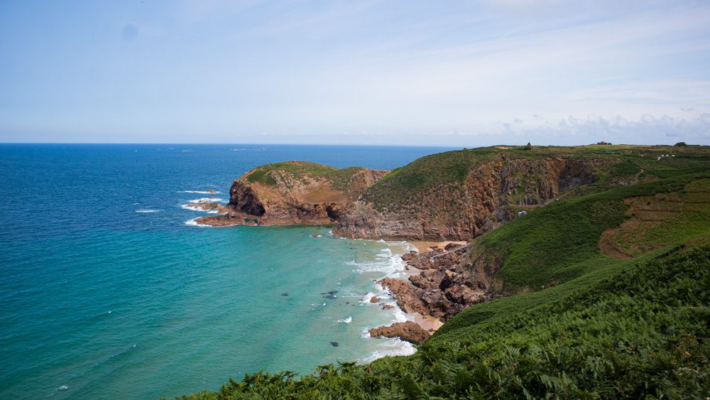 Plemont Bay with green cliffs and golden sandy bay the turquoise blue sea off to the left