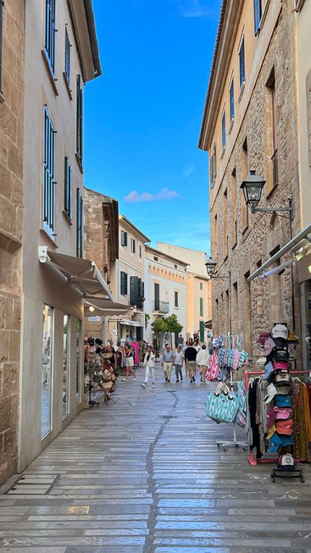 Narrow street in Alcudia old town with shops to the sides selling bags, hats etc