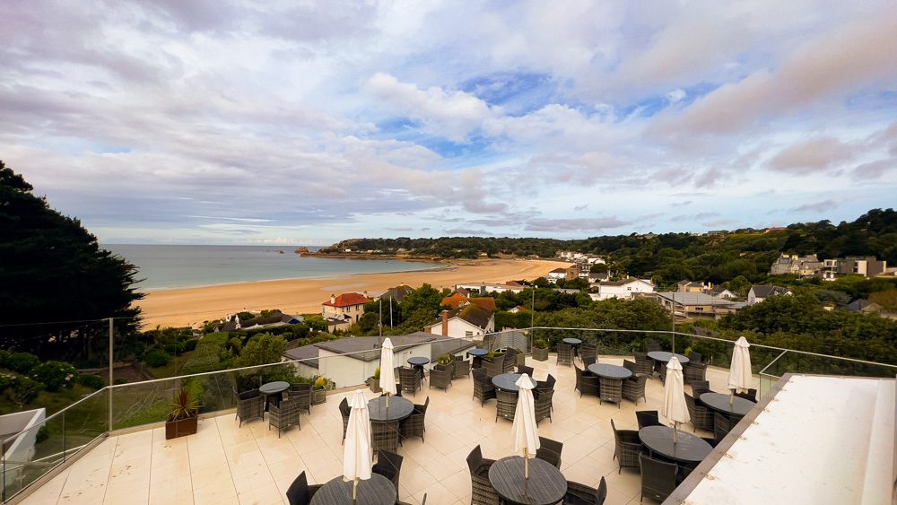 black wicker chairs around matching tables with white sun umbrellas on the terrace at the Biarritz Hotel overlooking St Brelade's Bay