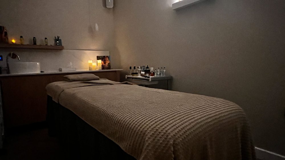 massage bed with beige covering and bottles of oils to the side. The room is lit by candlelight