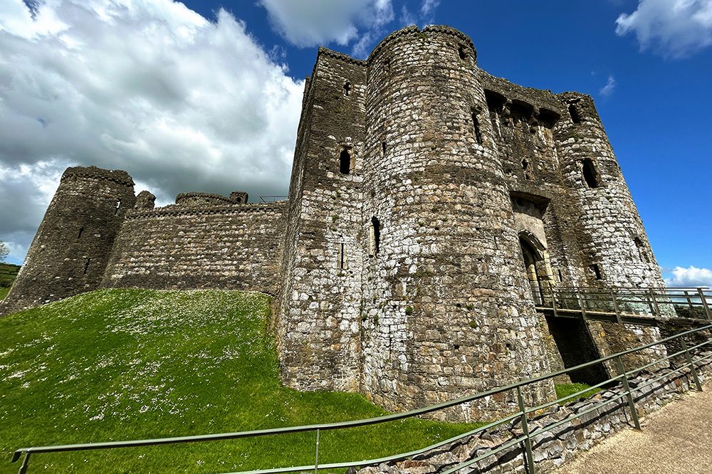 Kidwelly Castle standing on a grassy mound against a blue sky