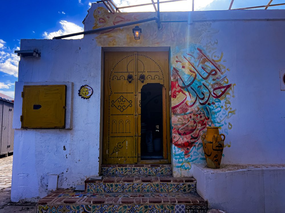 The outside of Arceram with a yellow door studdied with black studs. Bright Arabic writing around the door