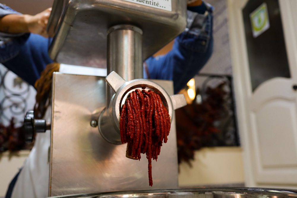 The bright red harissa coming out of the grinder in long thin stips