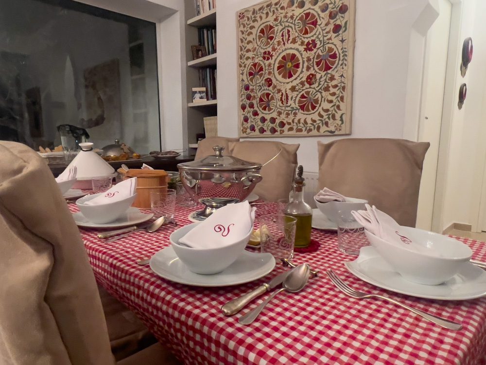 table with red gingham table cloth and white crockery. There is a silver pot, olive oil and on the sideboard has more silver platters