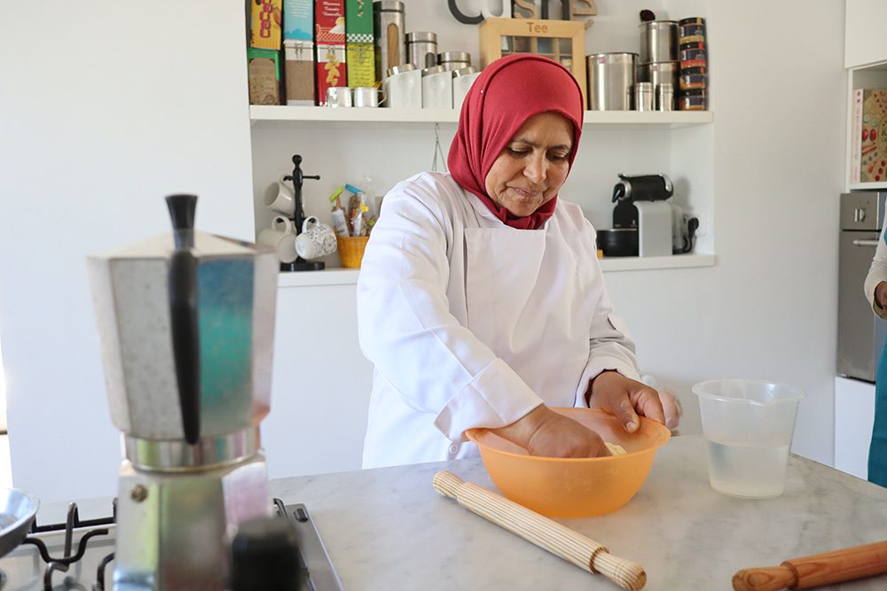 Lady called Moufida wearing a white apron and a red head scarf making mwali dough in an orange bowl