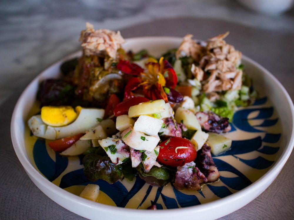Blue and white plate with salads including eggs, tuna, octopus