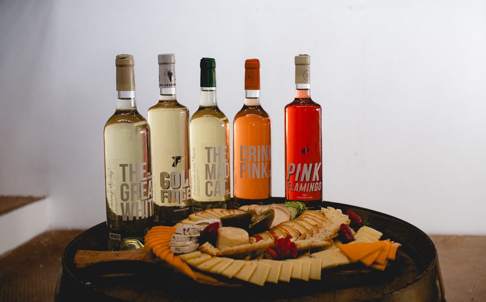 5 bottles of wine with a platter of cheeses in front of it